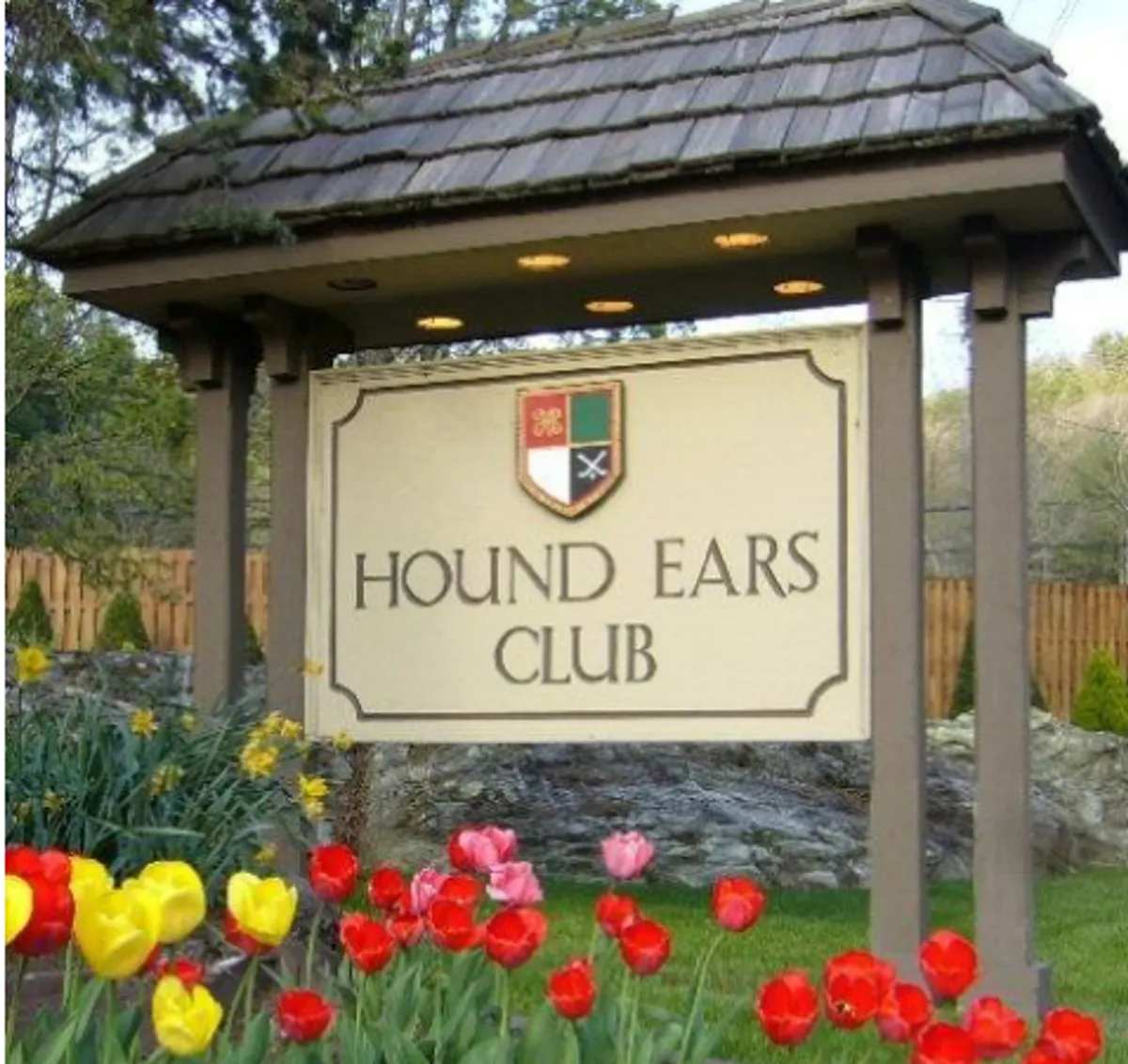 The image features the welcoming signage of the Hound Ears Club, surrounded by vibrant tulips and manicured landscaping. The entrance signifies exclusivity and hints at the secure, prestigious nature of the community. The lush plantings and maintained grounds suggest a peaceful, inviting atmosphere.