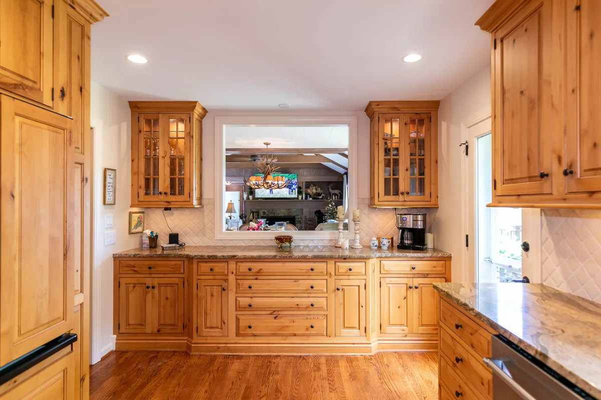 A cozy kitchen nook featuring wood cabinetry, a granite countertop, and a prominent coffee maker on the counter. The open window view and decorative items create a warm, inviting setting that highlights both the coffee bar and the kitchen’s everyday usability.