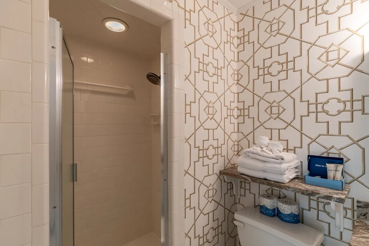 A spa-like ensuite bathroom with a modern geometric tile shower, neatly stacked towels, and a shelf with luxury toiletries. The space feels sophisticated and inviting, ideal for unwinding after a day of adventure.