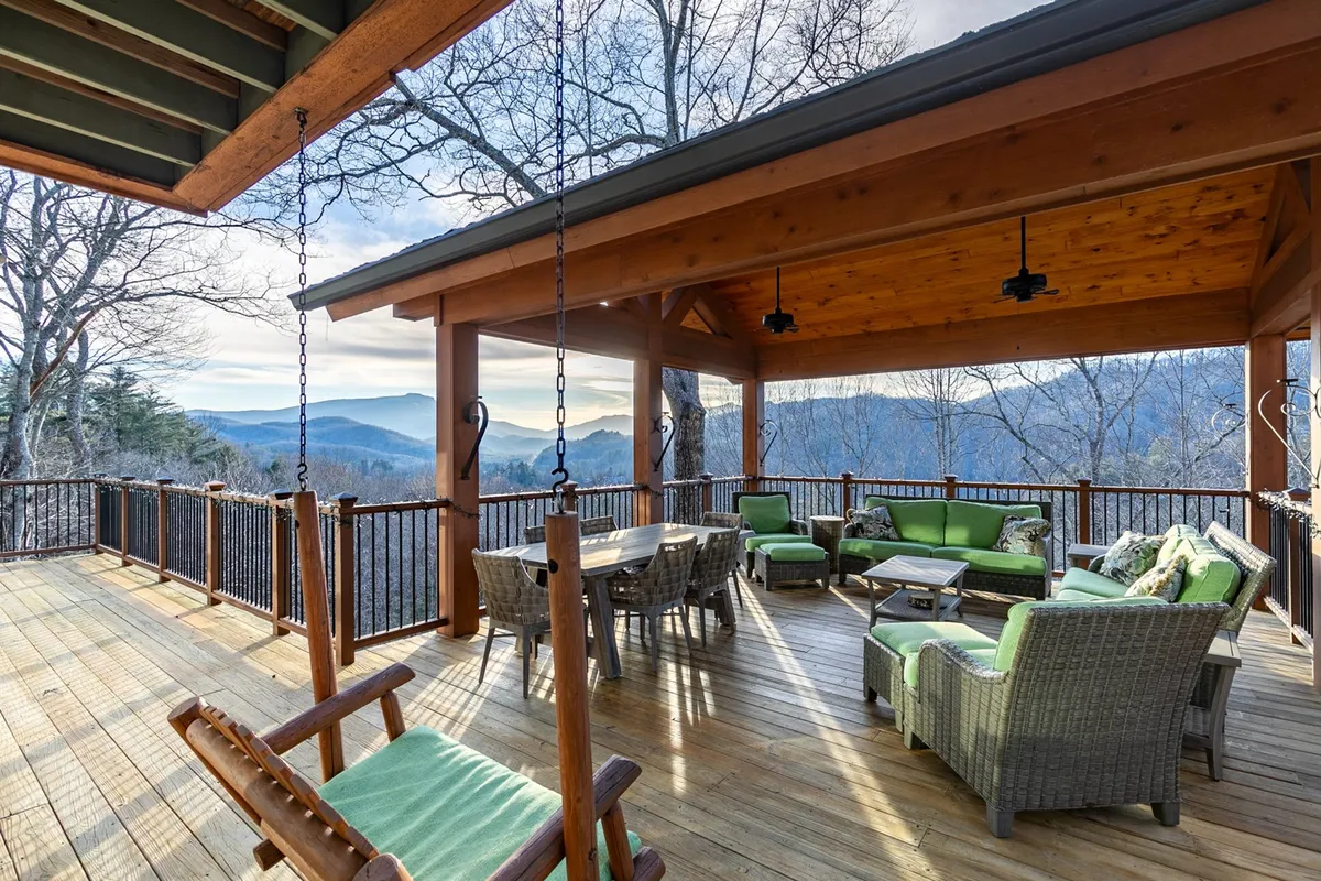 This exterior image showcases a welcoming porch seating area with comfortable furniture, a wooden swing, and breathtaking mountain views in the background. The setup suggests a tranquil space perfect for relaxing with pets after a day of adventure.