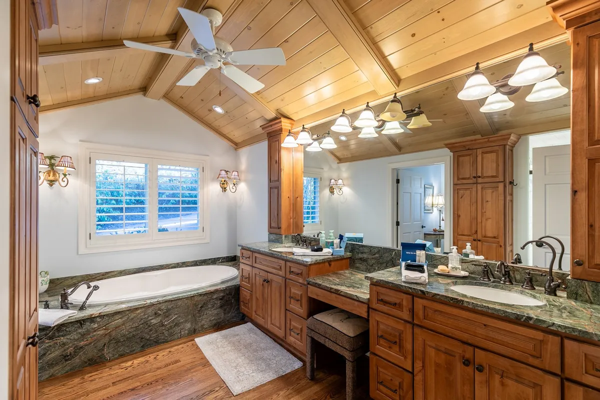 A tranquil ensuite bathroom featuring a freestanding bathtub, double sink vanity, warm wooden cabinetry, and soft decorative lighting. The space exudes a serene, luxurious hotel-like atmosphere.