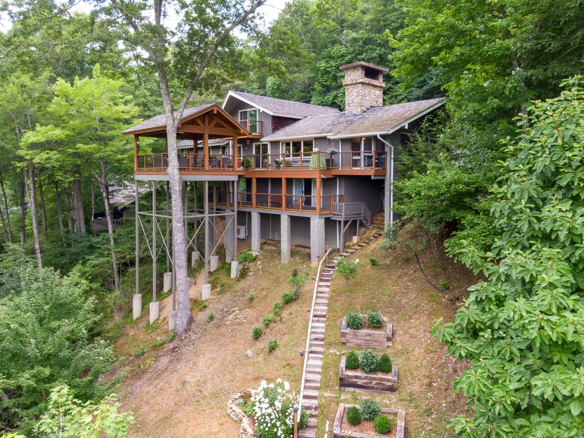This exterior image features an elevated deck with ample space for gatherings, a prominent stone chimney suggesting warmth and coziness, and a landscaped path inviting guests toward the house. The surrounding woods evoke the High Country’s natural beauty, perfect for adventure seekers returning from the slopes.