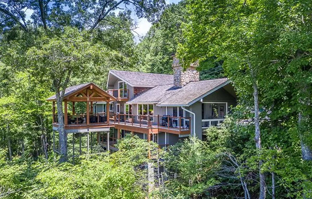 A wider exterior shot of the main house features the elevated deck surrounded by trees, set against a backdrop of natural beauty. The image captures moments such as morning coffee, sunset gatherings, and evenings under the stars, showing the porch as a true extension of the home.