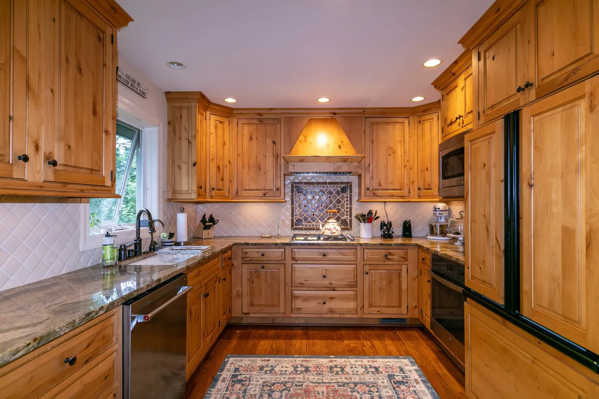 This image showcases a modern kitchen with granite countertops, wooden cabinetry, a decorative tile backsplash, and a prominent kitchen island. The space is clearly set up for meal preparation and social gatherings, with ample room for group activities and a welcoming, homely feel.
