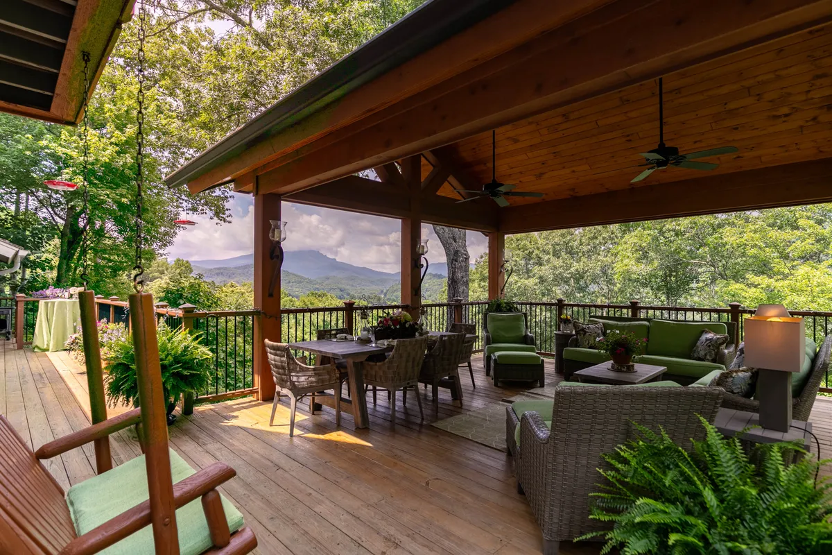 A spacious outdoor deck furnished with comfortable seating, offering sweeping mountain views and surrounded by lush greenery. The setting is perfect for relaxing, socializing, or simply soaking in the natural beauty of the area.