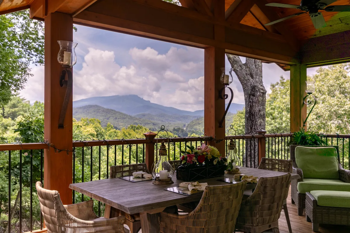 This exterior image showcases a dining table set up on a spacious porch, with comfortable seating and a sweeping view of the mountains and surrounding greenery. The scene feels tranquil and inviting, suggesting a perfect spot for al fresco meals, social gatherings, or quiet relaxation.