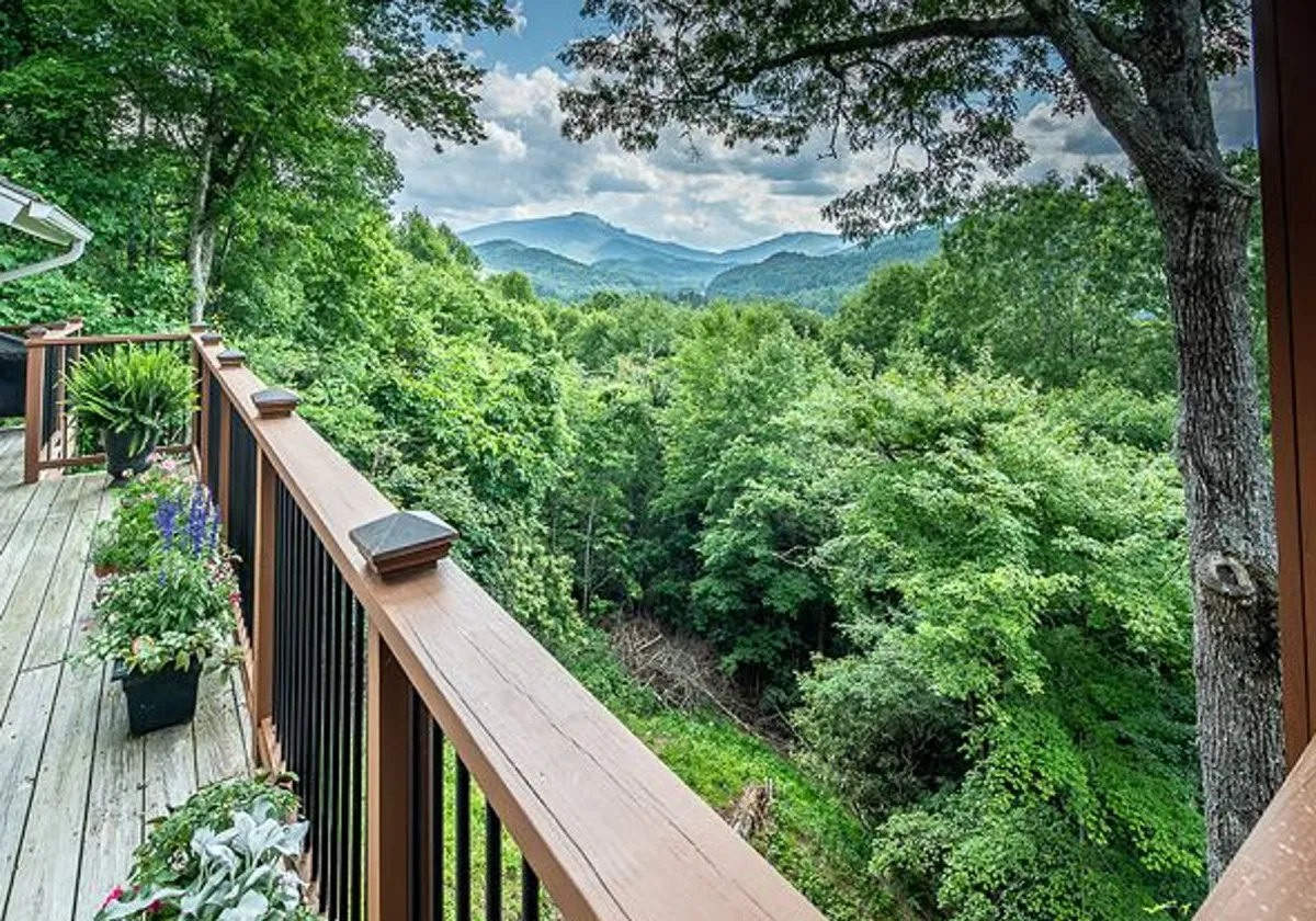 A panoramic view from a wooden deck overlooking lush greenery and dramatic mountains. Planters with flowers and comfortable seating make it a serene spot to soak in the surroundings, echoing the High Country's allure.