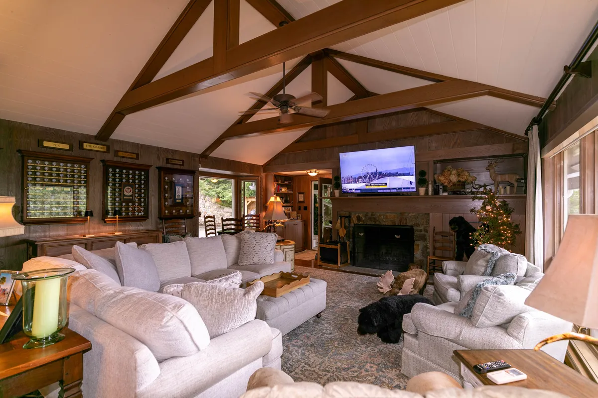 A comfortable den setup with a large sectional sofa facing a wall-mounted TV above a wood-burning fireplace. Decorative touches like a Christmas tree and mantel décor add warmth and showcase the room’s suitability for movie nights, holiday gatherings, and relaxing by the fire. The overall setting is intimate and inviting.